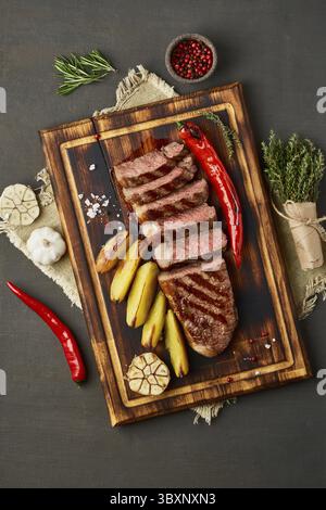 Régime keto cétogène steak grillé de bœuf frit, striploin, pommes de terre tranchées à bord de la table marron foncé. Recette de nourriture Paleo avec morceau haché de Banque D'Images