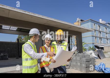 Les ingénieurs collaborent sur des plans de construction en extérieur, mettant l'accent sur le travail d'équipe et le développement pour le projet Banque D'Images