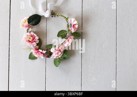 Vue de dessus de la couronne de fleurs roses textiles repose sur une table en bois blanc. Gros plan. Copier l'espace Banque D'Images