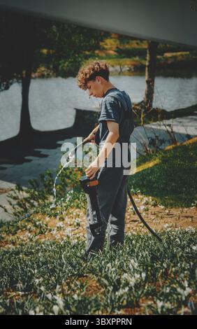 jeune jardinier avec un tuyau dans la main marche sur l'herbe Banque D'Images
