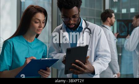 Deux médecins discutant des résultats de l'examen médical du patient femme caucasien thérapeute médecin parler avec l'homme afro-américain chirurgien médecin travail d'équipe Banque D'Images