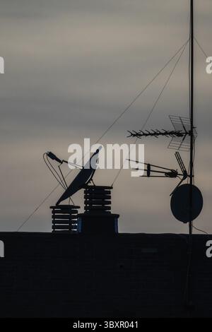 Silhouette de différentes antennes et antennes paraboliques montées sur un toit au crépuscule ou à l'aube. Ciel nuageux. EQUIPEMENT de télécommunications Banque D'Images