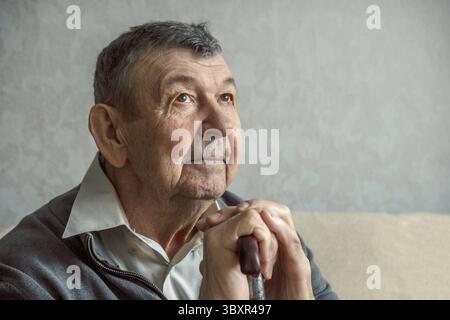 Portrait d'homme âgé triste sur fond gris. Regard réfléchi de vieux aînés assis seul à la maison. Gros plan du visage froissé, espace de copie. Banque D'Images