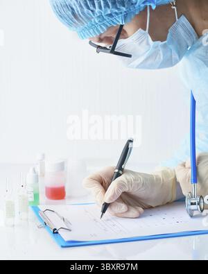 Pandémie COVID-19, Coronavirus. Le médecin de l'hôpital est en service, il est disponible pour le travail et remplit les formulaires. Une femme en uniforme et un masque facial effectuent des tests en laboratoire Banque D'Images