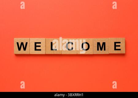 Mot Bienvenue fait de cubes en bois sur fond rouge, vue de dessus Banque D'Images