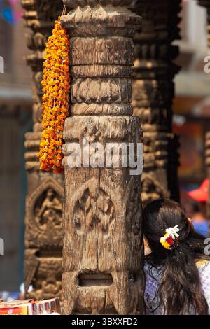 6 avril 2013, Patan, province de Bagmati, Népal : une femme est assise à côté d'un pilier en bois sculpté avec une guirlande de fleurs sur un vieux bâtiment à Patan, au Népal. (Crédit image : © Jon G. Fuller/VW pics via ZUMA Press Wire) Banque D'Images