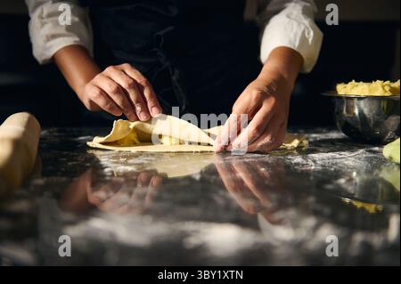 Gros plan des mains préparant la pâte à pâtes pour les raviolis sur une surface farinée, avec une ambiance chaleureuse et artisanale mettant en lumière les traditions culinaires italiennes. Captur Banque D'Images