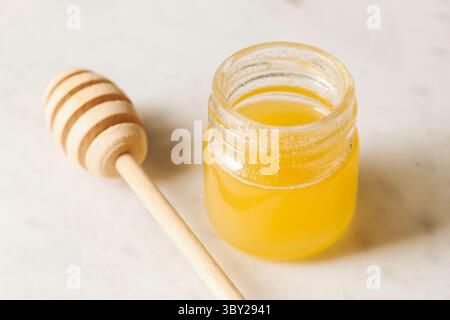 Miel frais dans un bocal en verre. Douceur naturelle avec un plongeur de miel sur fond de marbre. Produit biologique sain riche en nutriments. Texture liquide dorée Banque D'Images