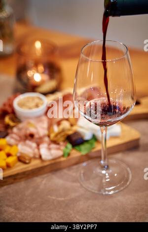 Un verre de vin rouge est versé, accompagné d'une planche de charcuterie avec du fromage, des viandes et des noix, créant un cadre élégant pour dîner. Banque D'Images