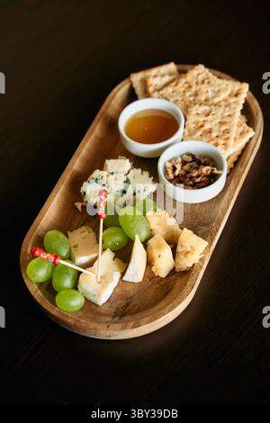 Un élégant plateau de fromages comprend un assortiment de fromages gastronomiques, de noix, de raisins verts et de miel, servis sur un plateau en bois avec des craquelins, parfait pour une sa Banque D'Images