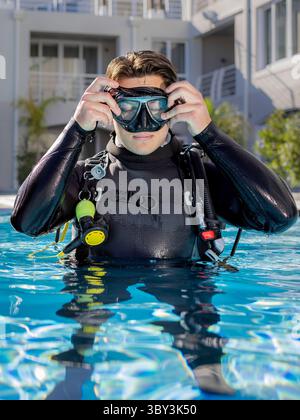 Un plongeur dans une piscine d'un centre de plongée, portant une combinaison complète et un équipement de plongée, enfilant son masque de plongée Banque D'Images