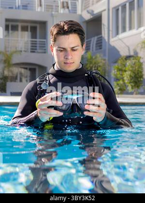 Un plongeur dans une piscine d'un centre de plongée, portant une combinaison complète et un équipement de plongée, rince son masque de plongée Banque D'Images