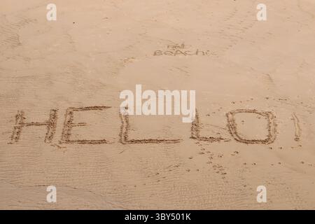 Un « Bonjour ! » Salutation écrite en majuscules sur une plage de sable à marée basse avec un plus petit 'Hello Beach !' salutation écrite ci-dessus Banque D'Images