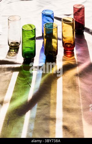 Des verres colorés projettent de longues ombres colorées sur la nappe Banque D'Images