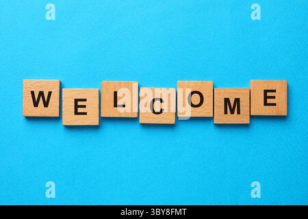 Word Welcome fait de cubes en bois sur fond bleu clair, vue de dessus Banque D'Images