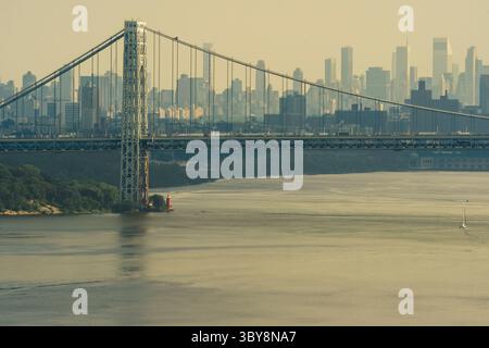 New York, NY - US - Jul 2, 2025 le pont George Washington enjambe le fleuve Hudson avec la ligne d'horizon de New York dans un arrière-plan brumeux. Ci-dessous, l'emblématique illuminé Banque D'Images