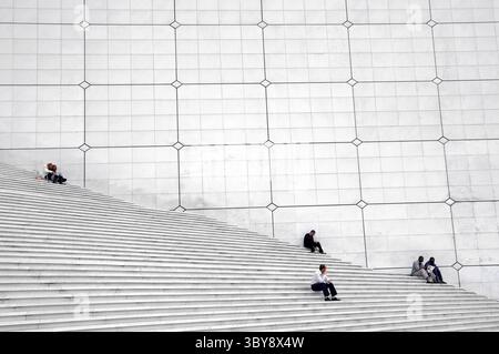 Les gens assis se sont étendus sur un grand escalier symétrique en béton, Paris, France Banque D'Images