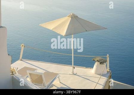 Grèce. Une soirée d'été tranquille à Santorin. Deux chaises longues et un parasol sur le balcon avec vue sur la mer Banque D'Images