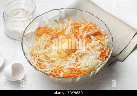 Nourriture, Un bol en verre rempli de chou blanc râpé et de carottes râpées, avec un œuf cru craqué au centre pour une crêpe aux légumes maison ou fr Banque D'Images