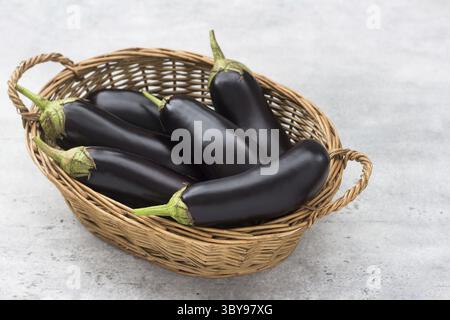 Nourriture, panier en osier avec aubergines mûres et herbes sur un fond texturé gris Banque D'Images