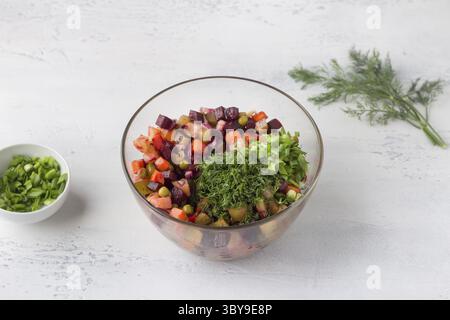 Nourriture, bol en verre avec salade de vinaigrette de légumes, betteraves, carottes, pommes de terre, pois verts en conserve et oignons rouges sur fond bleu clair. Cuisine Banque D'Images