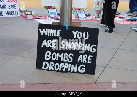 Un panneau indiquant « pendant que vous magasinez des bombes tombent » est vu lors d’une manifestation organisée par Burbank pour la Palestine, le 16 juillet 2025. Banque D'Images