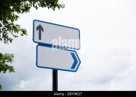 Un double panneau de direction bleu contre un ciel blanc clair contenant des flèches vers le haut et latérales avec des lettres supprimées pour être modifiable pour l'image conceptuelle. Banque D'Images