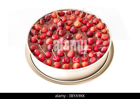 Un gâteau rond fraîchement fait maison garni de sauce coulis et de fraises entières et de cerises, placé dans un moule en métal. Vue oblique de dessus. Banque D'Images