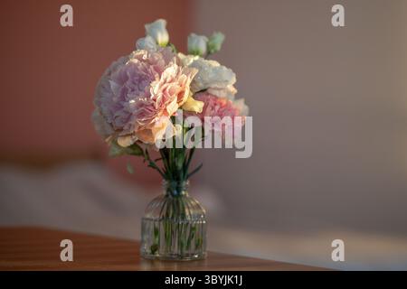 Bouquet compact d'œillet de pivoine lisianthus dans un vase clair sur une table ensoleillée. Arrangement de fleurs Banque D'Images
