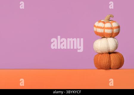 Citrouilles tricotées blanches et oranges sur fond violet, vue de face. Concept d'Halloween. Jouets tricotés faits à la main pour enfants et décoration de maison de vacances. Banque D'Images