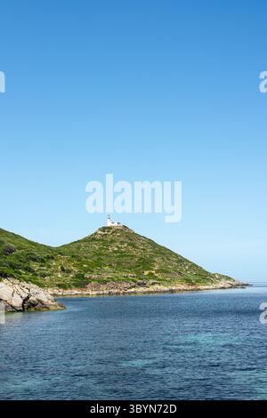 Une vue côtière sereine sur une colline verdoyante à Turkiye, avec un phare au sommet, sous un ciel bleu clair et des eaux calmes. Banque D'Images