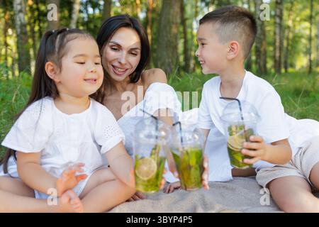 Heureux pique-nique familial en été mère de la nature et les enfants souriant avec de la limonade profitant du temps en plein air ensemble Banque D'Images