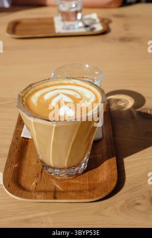 Blanc plat servi sur un plateau en bois, accompagné d'un verre d'eau et d'un petit biscuit, placé sur une table dans un café moderne andorran. Banque D'Images