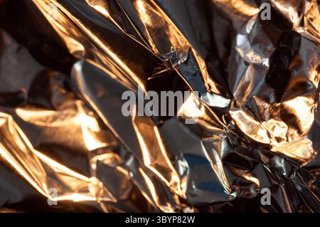 Gros plan d'une feuille d'aluminium froissée réfléchissant la lumière et créant un jeu dynamique d'ombres et de lumières Banque D'Images