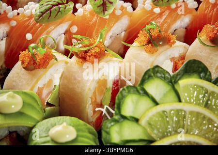 Gros plan dynamique de rouleaux de sushi assortis avec saumon, avocat et mamenori, garnis de tobiko, concombre et tranches de citron vert. Style asiatique populaire Banque D'Images