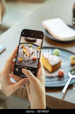 Femme à l'aide d'un smartphone prenant photo de délicieux gâteau sur l'assiette dans le restaurant Banque D'Images