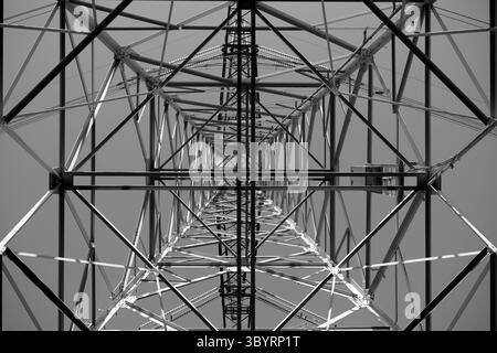 En regardant à travers la toile d'acier d'un pylône de transmission haute tension imposant, on découvre une géométrie de treillis complexe qui s'envole dans un ciel bleu clair aujourd'hui. Banque D'Images