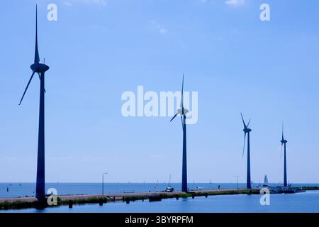 Quatre éoliennes se tiennent sur une jetée étroite d'Amsterdam au-dessus de l'eau calme sous un ciel dégagé, symbolisant tranquillement l'innovation néerlandaise dans les énergies renouvelables propres Banque D'Images