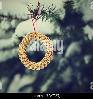 Belles décorations de Noël naturelles en paille sur un arbre de Noël enneigé. Fond extérieur coloré de la nature d'hiver pour les vacances Banque D'Images