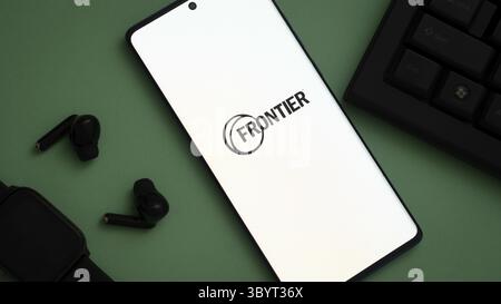 Smartphone affichant le logo Frontier, entouré d'un fond vert avec des accessoires technologiques Banque D'Images