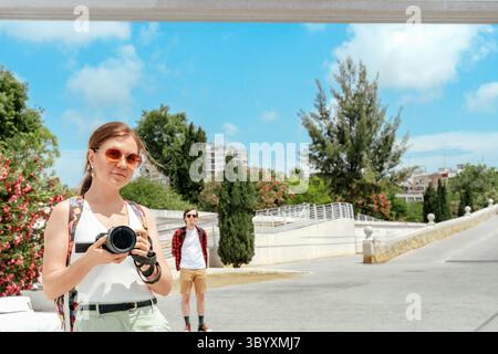 Femme souriante avec appareil photo dans les mains prenant photo selfie avec partenaire en vacances en plein air dans le parc verdoyant ensoleillé à Valence, espace de copie Banque D'Images
