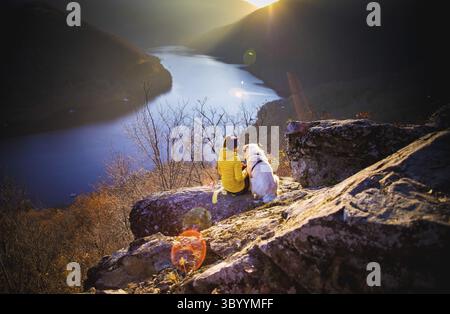 Femme et son chien assis sur le rocher profitant d'une vue d'automne incroyable sur le lac au coucher du soleil Banque D'Images