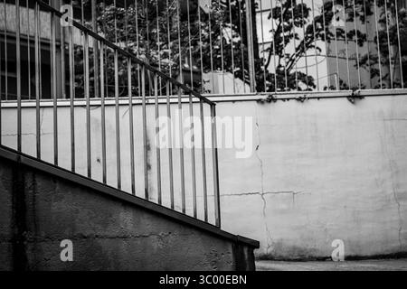 Photo minimaliste en noir et blanc d'une rampe d'escalier et d'un mur en béton avec des fissures visibles, créant des lignes fortes et un contraste urbain. Banque D'Images