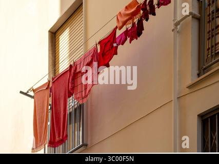 Le linge coloré rouge et orange est suspendu à une ligne de lavage à l'extérieur d'un bâtiment peint en terre cuite en Italie. Une scène typique de ville italienne. Banque D'Images