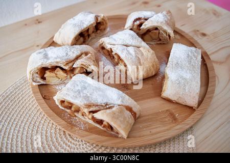 Lamelles de strudel de pomme brun doré recouvertes de sucre en poudre sur un plateau en bois. Un régal alléchant pour les amateurs de desserts. Banque D'Images