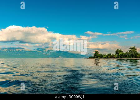 Lac Ohrid avec montagnes et arbres riverains en Albanie sous ciel bleu Banque D'Images