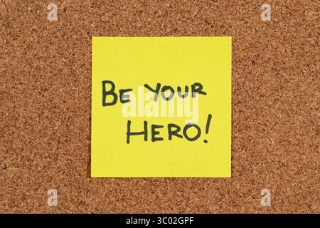 Gros plan sur une note collante avec une phrase de motivation positive « soyez votre héros » sur un fond de liège Banque D'Images