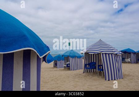 Des tentes de plage rayées avec des chaises en plastique parsèment la rive sablonneuse de la Praia da Claridade Banque D'Images