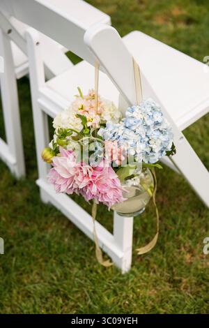 Fleurs de cérémonie pastel suspendues sur la chaise de mariage blanche Banque D'Images
