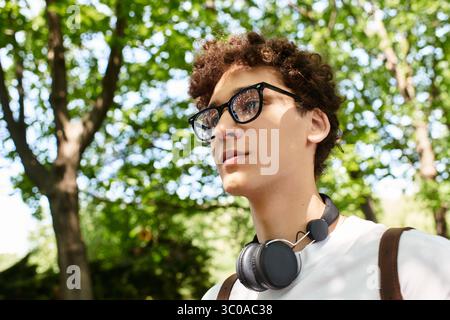 Un jeune homme aux cheveux bouclés se détache dans un parc d'été dynamique rempli de verdure. Banque D'Images